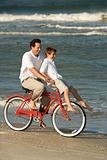 Dad riding bike with son on handlebars.