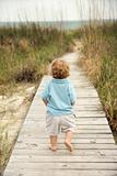 Little boy walking down beach walkway.