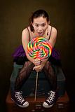 Pretty girl in funky purple outfit on green background with big lollipop
