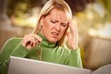 Grimacing Woman with Glasses Using Laptop Suffering a Painful Headache.