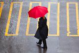woman with red umbrella walking on pedestrian crossing in rain