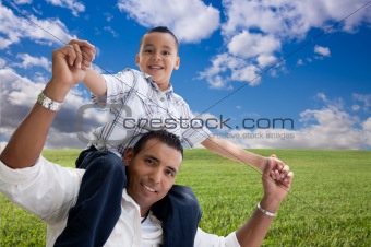 Happy Hispanic Father and Son Over Grass Field, Clouds and Blue Sky.