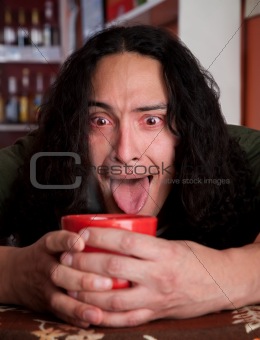 Tired Latino man cradling red coffee cup