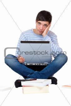 Young handsome pupil sitting frustrated on floor with books and laptop
