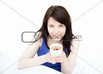 Jolly woman drinking a coffee sitting on her bed