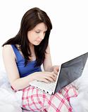 Concentrated woman using a laptop sitting on bed