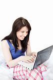 Laughing woman using a laptop sitting on bed