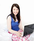 Radiant woman using a laptop sitting on bed