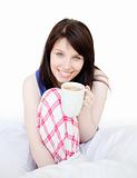 Brunette woman drinking coffee sitting on bed