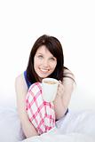 Mirthful woman drinking coffee sitting on bed