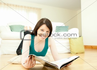 Brunette woman reading a magazine lying down on the floor