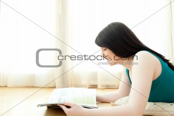 Interested woman reading a magazine lying down on the floor