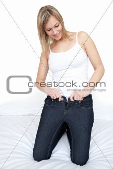 Beautiful woman putting on tight jeans on a bed