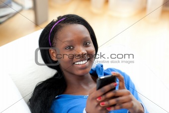 Bright woman sending a text lying on a sofa