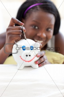 Cheerful teen girl putting money in a piggy-bank 