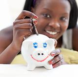 Smiling teen girl putting money in a piggy-bank 