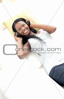 Cheerful woman listening music with headphones lying on a sofa