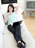Young woman shopping on-line lying on a sofa 