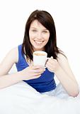 Smiling attractive woman drinking a coffee sitting on her bed