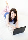 Joyful woman surfing the internet lying on a bed