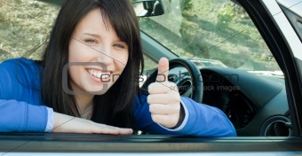 Happy teen girl with a thumb up sitting in her car 