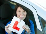 Joyful teen girl sitting in her car tearing a L-sign