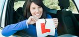 Smiling teen girl sitting in her car tearing a L-sign