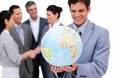 Cheerful businessman holding a globe in front of his team 