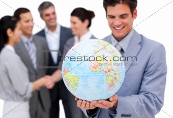 Cheerful businessman holding a globe in front of his team 