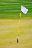 three golf balls on the putting green surrounding hole with a flag