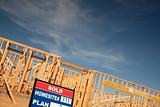 Sold Lot Real Estate Sign at New Home Framing Construction Site Against Deep Blue Sky.