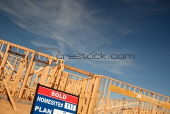Sold Lot Real Estate Sign at New Home Framing Construction Site Against Deep Blue Sky.