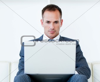 Concentrated businessman using a laptop sitting on a sofa