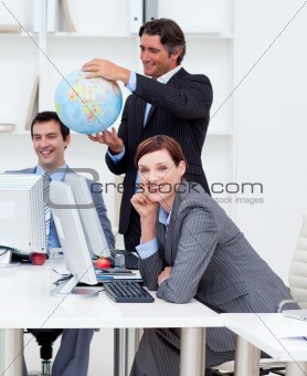 Happy manager holding a globe with his team working at computers