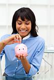 Enthusiastic ethnic businesswoman saving money in a piggybank 