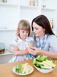 Annoyed blond girl eating vegetables with her mother