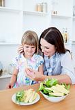Brunette mother helping her daughter prepare salad in the kitchen