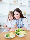 Cute little girl eating vegetables with her mother