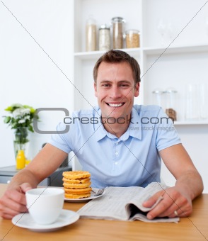 Attractive man reading a newspaper while having breakfast