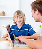 Cute boy having breakfast while his father using a laptop