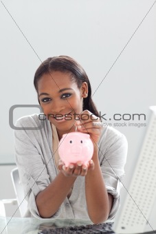 Confident ethnic businesswoman saving money in a piggybank 