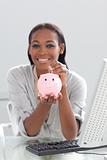 Smiling ethnic businesswoman saving money in a piggybank 