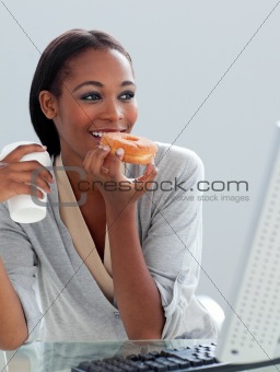 Ethnic businesswoman eating a donut at her desk 