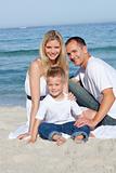 Portrait of cheerful parents with their son sitting on the sand 