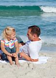 Adorable little girl and her father sitting on the sand