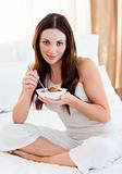 Brunette woman eating cereals sitting on bed