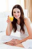 Brunette woman drinking orange juice on bed
