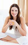 Jolly woman drinking orange juice on bed