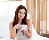 Relaxed woman drinking coffee sitting on bed