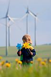 boy with long hair holding pinwheels standing in front of wind turbines